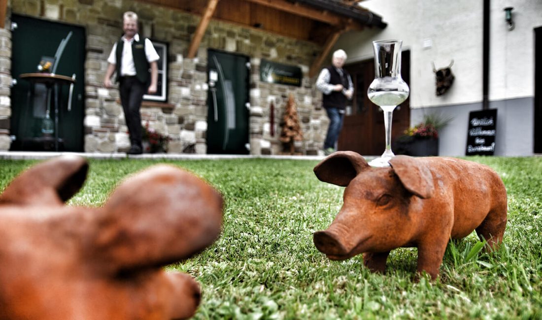 Auf einem kleinen Holzschwein wird auf der Wiese vor der Schnapsbrennerei ein Schnapsglas balanciert.