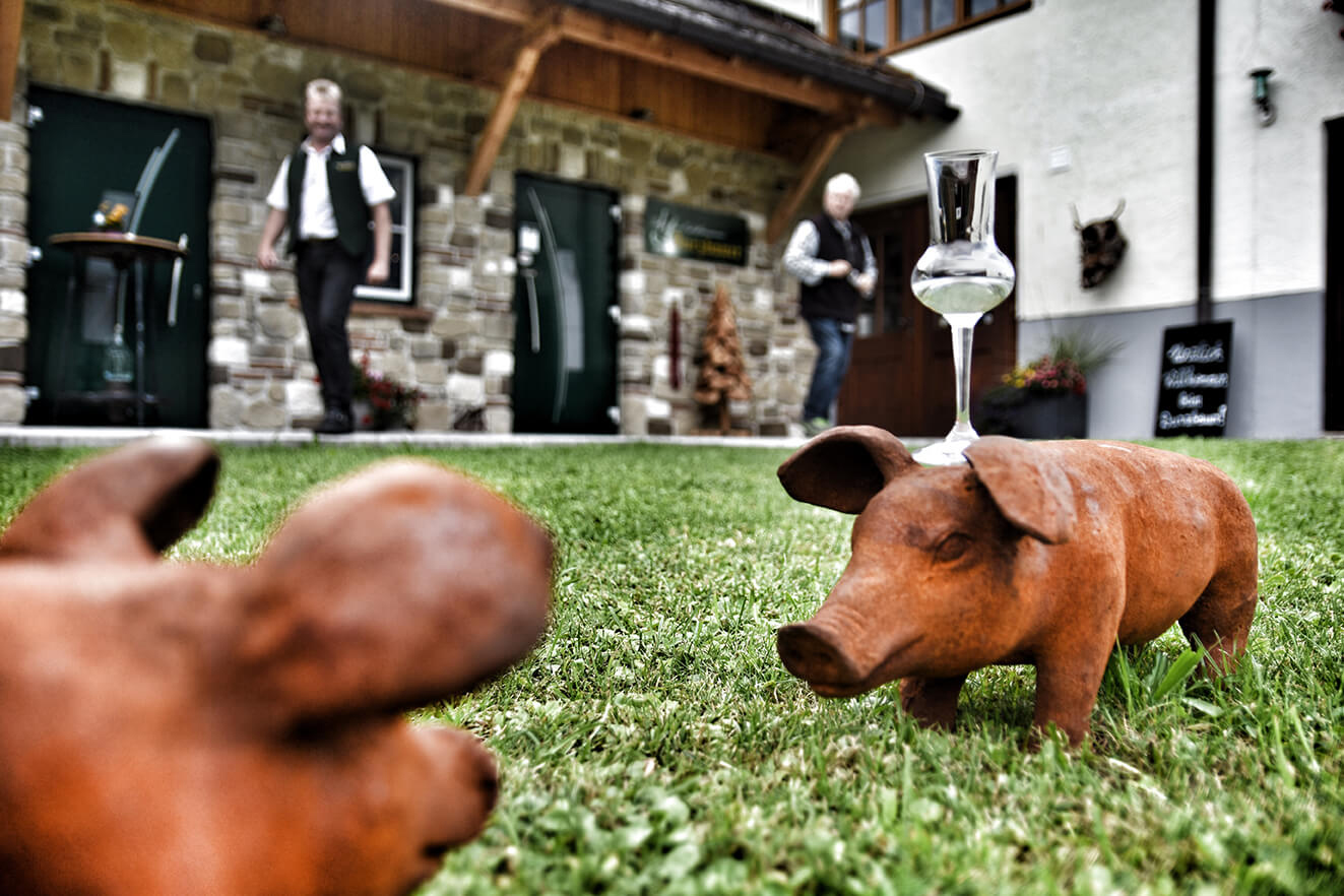 Auf einem kleinen Holzschwein wird auf der Wiese vor der Schnapsbrennerei ein Schnapsglas balanciert.