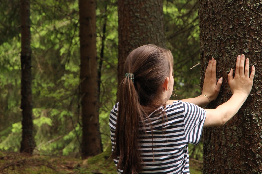 ein Mädchen berührt einen Baumstamm