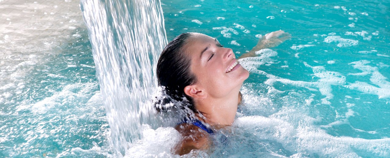 Dame im Thermalwasserbecken unter einem kleinen Wasserfall