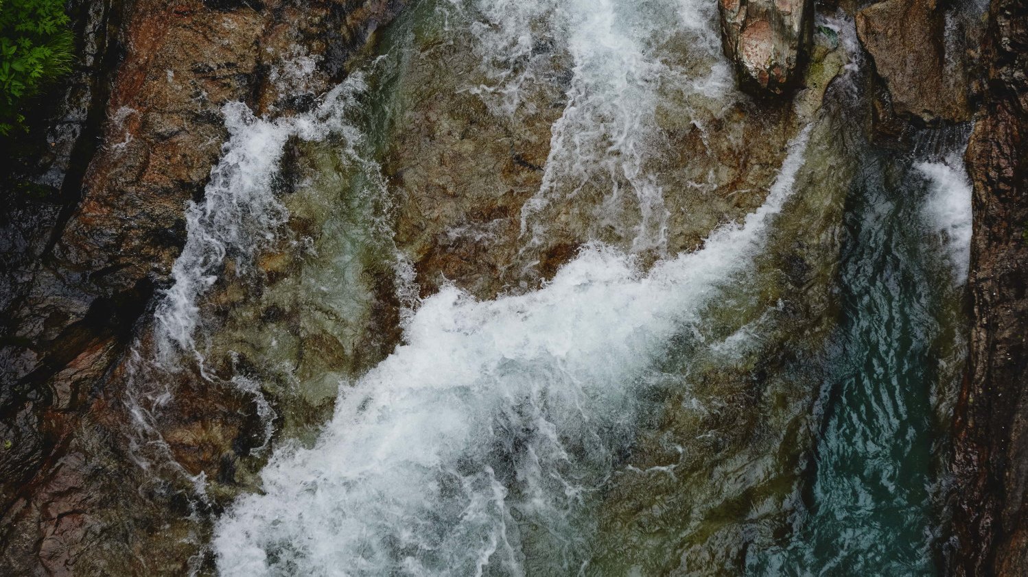 Ein klarer Gebirgsfluss fließt über glatte Steine, während schäumendes Wasser die Felsen umspült und spritzt.