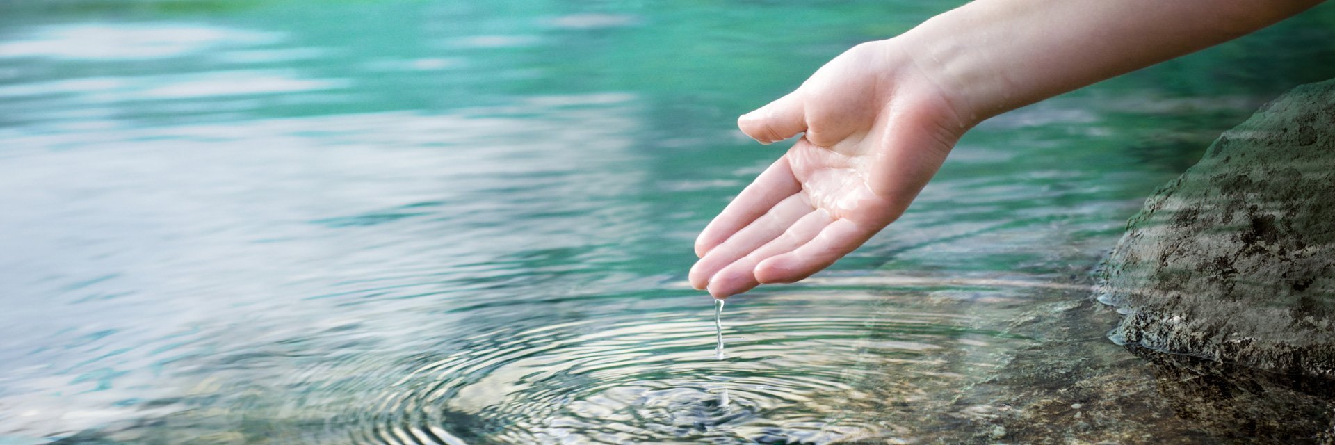 Hand einer Person vor der Wasseroberfläche eines Sees
