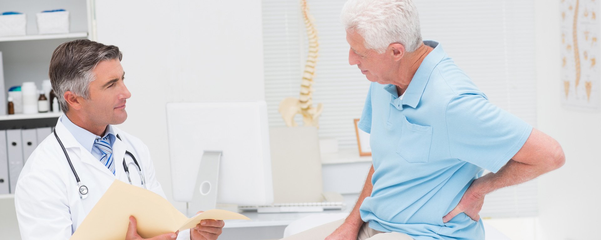 Patient sitzt auf der Liege beim Arzt und greift sich auf den Rücken