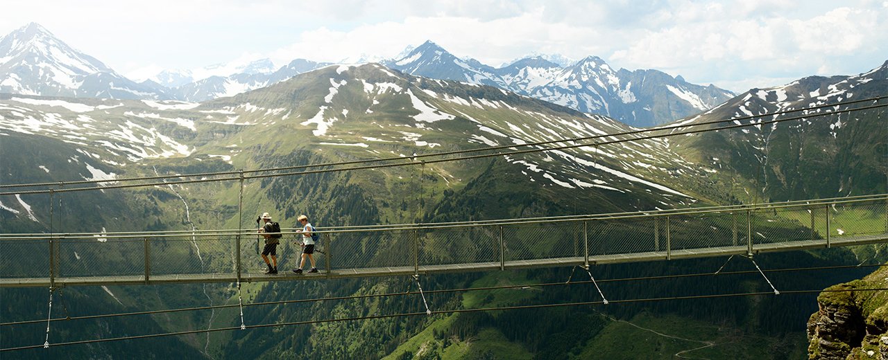 Zwei Wander*innen auf der Hängebrücke am Stubnerkogel mit Blick auf die Hohe Tauern in Bad Gastein.