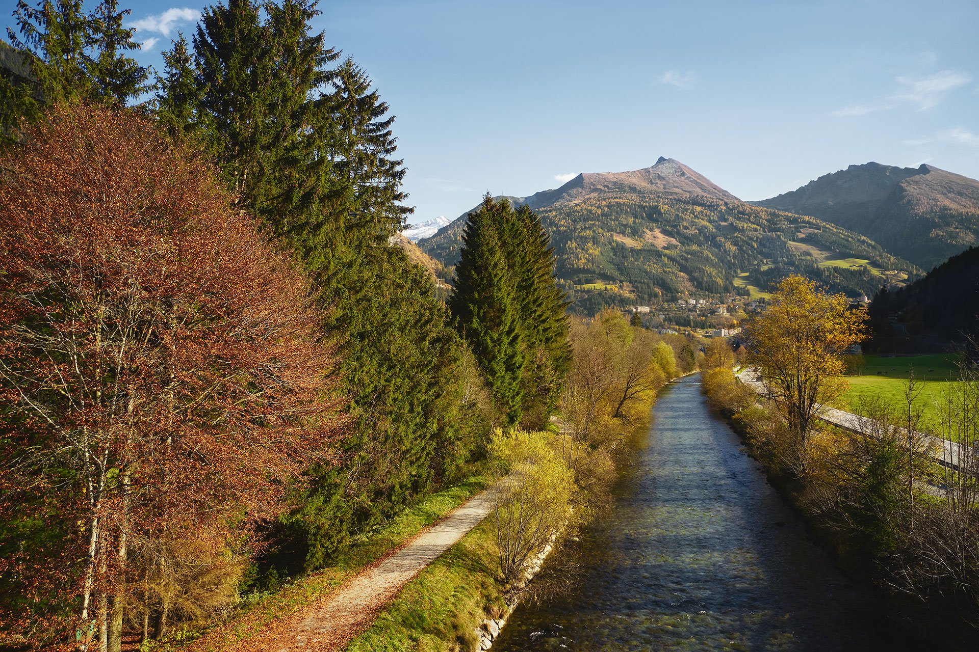 Ein ruhiger Fluss schlängelt sich durch eine herbstliche Landschaft, umgeben von hohen Bäumen und sanften Hügeln.