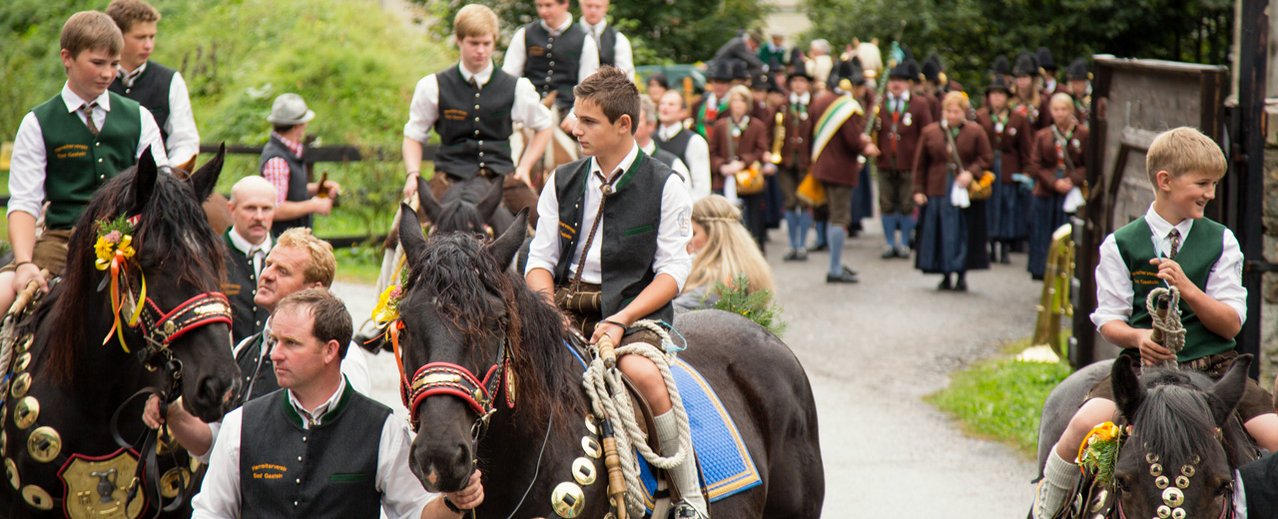 Kinder in Tracht auf Pferden, geführt von Aufsichtspersonen
