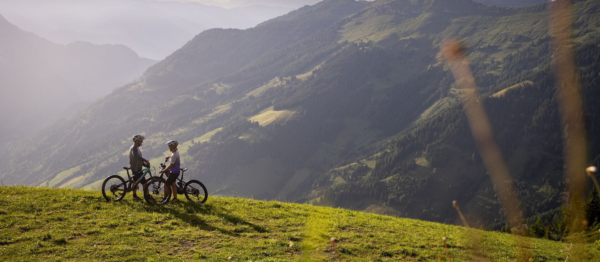 Zwei Mountainbiker stehen nebeneinander und blicken auf die beeindruckende Berglandschaft, die in sanften Farben leuchtet.