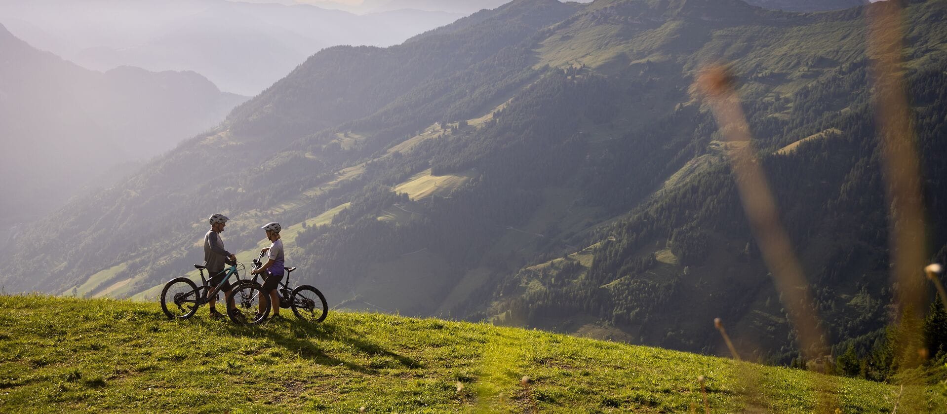 Zwei Mountainbiker stehen nebeneinander und blicken auf die beeindruckende Berglandschaft, die in sanften Farben leuchtet.