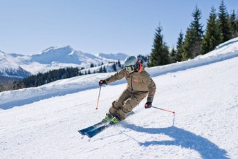 Skifahrerin beim Carven auf der Schlossalm im Gasteinertal mit Blick auf verschneite Alpen und Tannenwald
