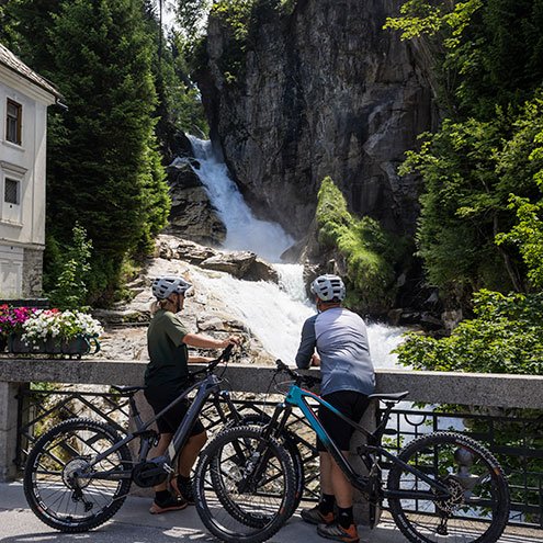 Zwei Mountainbiker*innen vor einem Wasserfall mit ihren Fahrrädern im Gasteinertal.