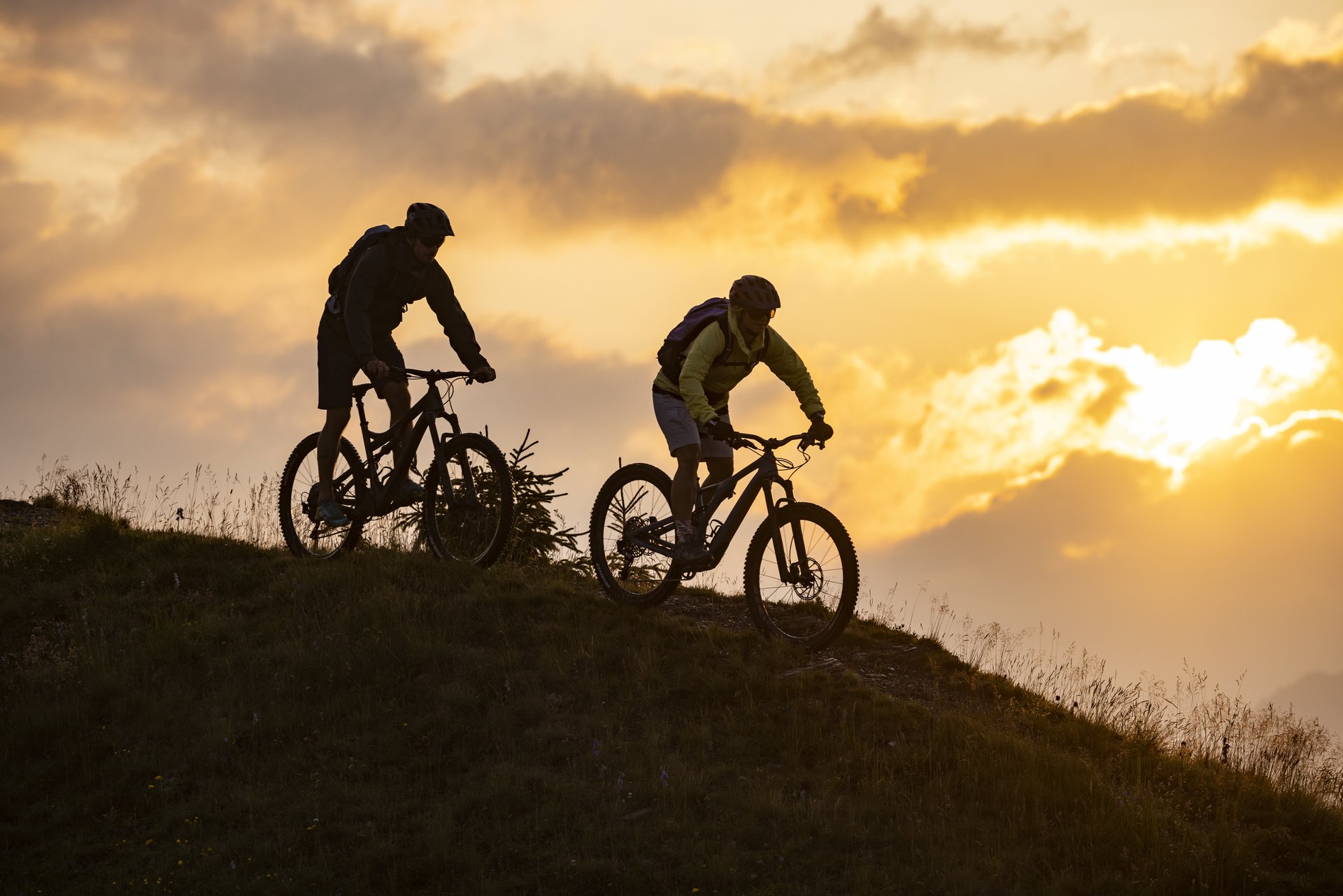 Zwei Mountainbiker auf einem Hügel vor dramatischem Sonnenaufgang in Gastein.