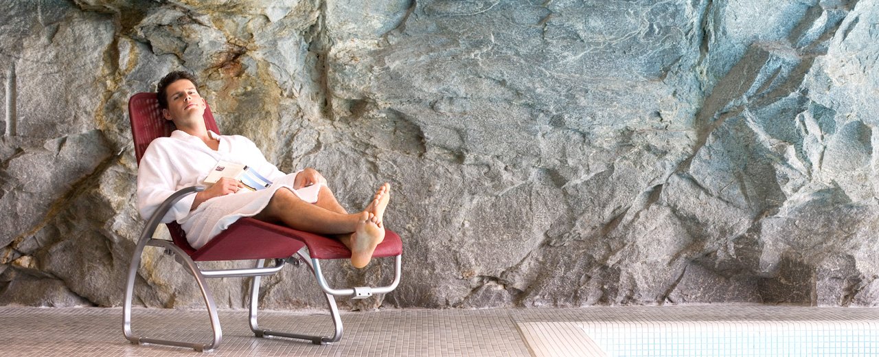 Mann beim Entspannen auf einer Liege vor der Felswand im Innenbereich der Felsentherme
