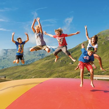 Kinder springen auf einem Hüpfkissen mit Bergpanorama auf der Schlossalm in Bad Hofgastein.