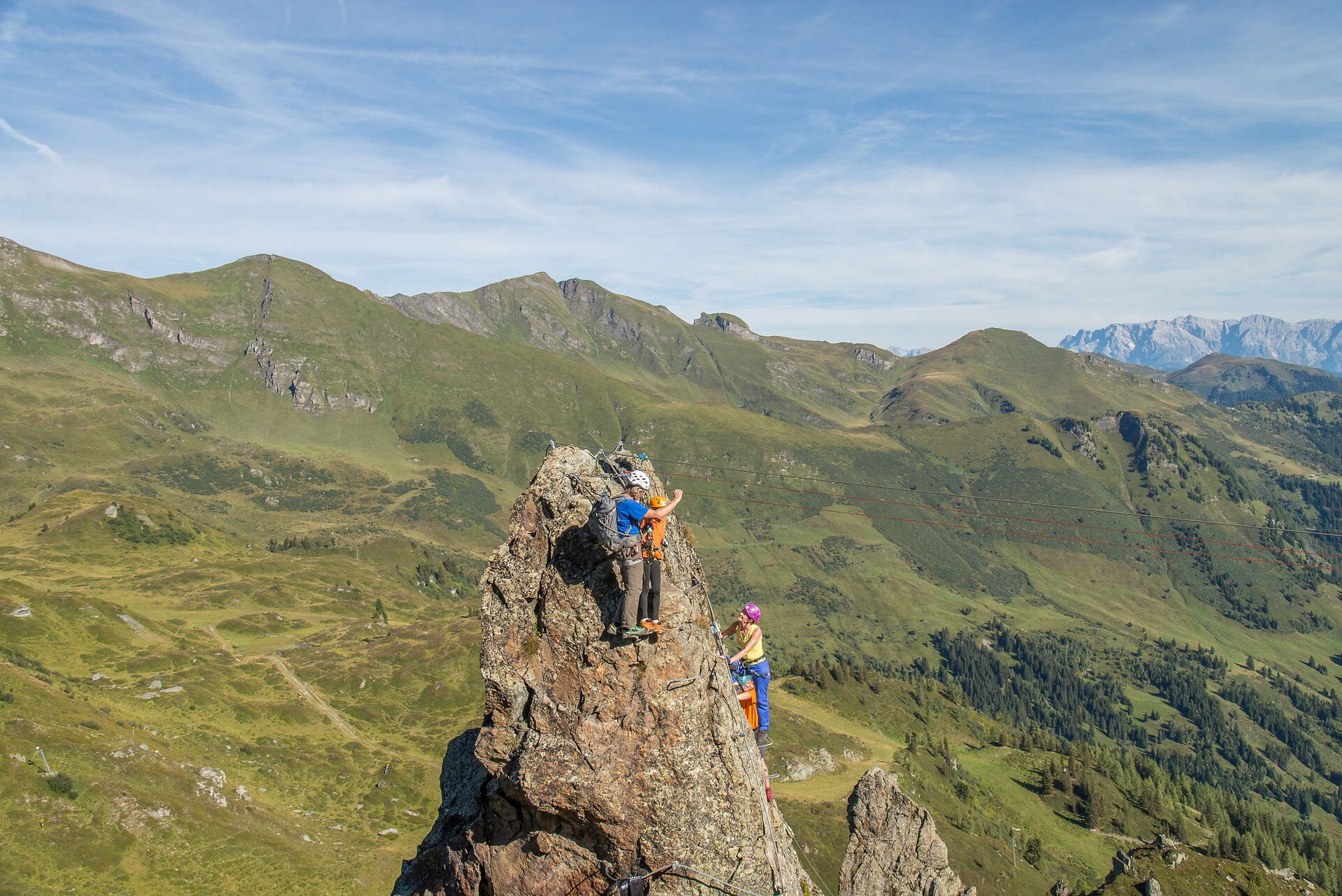 Die Szene zeigt zwei Kletterer, die in einer atemberaubenden Berglandschaft an einem Felsen klettern, umgeben von Natur.