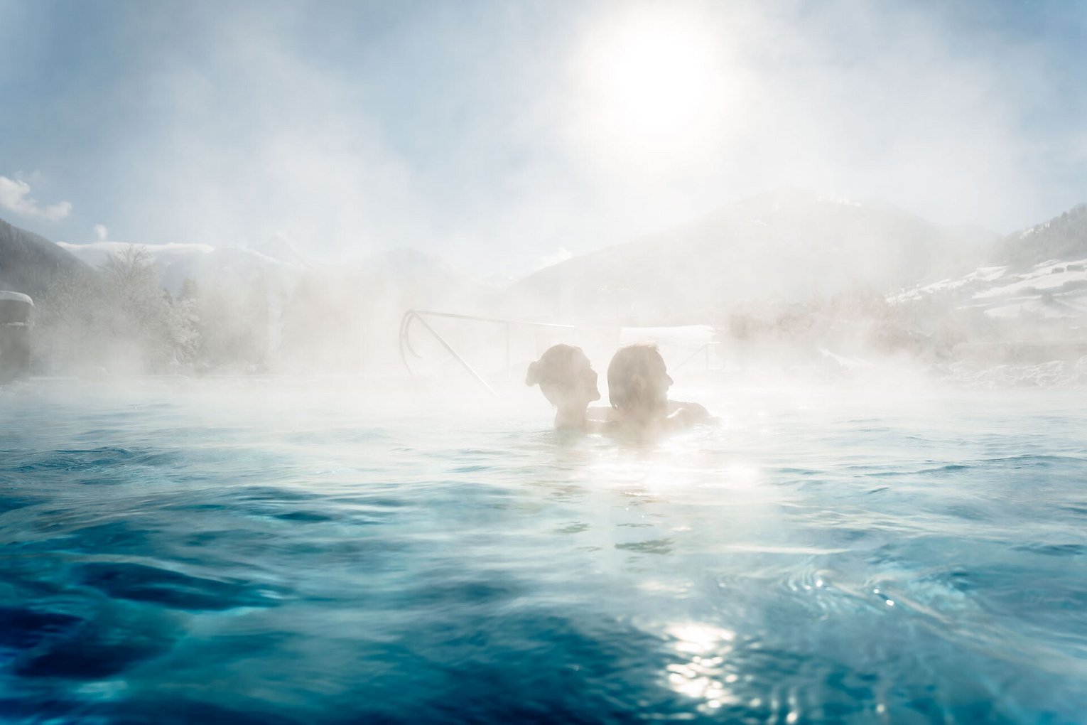 Menschen entspannen im warmen Außenbecken der Alpentherme Gastein mit Blick auf die verschneiten Berge.