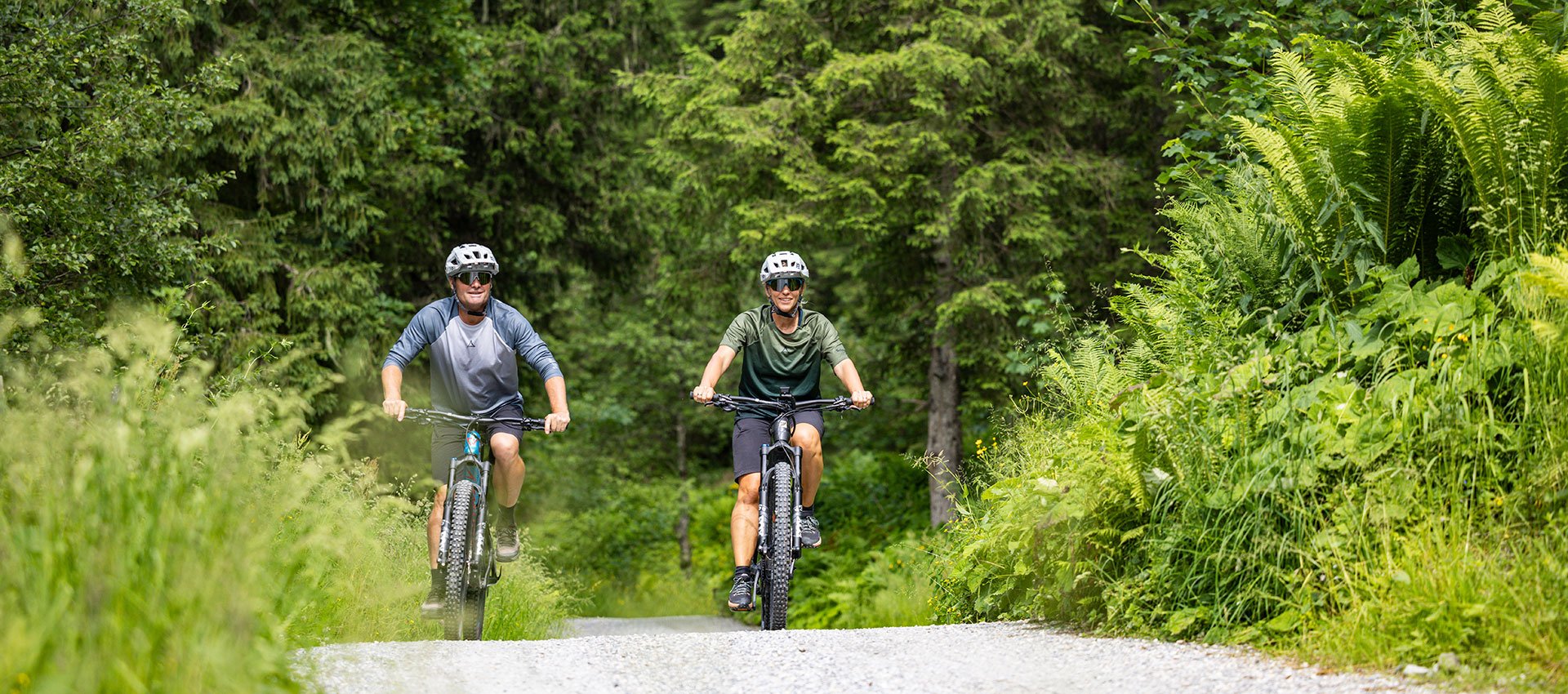 Zwei Mountainbiker auf einem Waldweg zwischen dichtem Grün in Gastein.