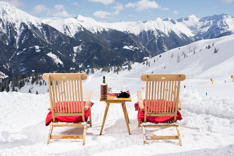 Zwei Liegestühle im Schnee mit Tisch und Wein vor verschneiter Berglandschaft im Gasteinertal.