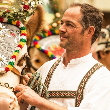 Mann in Tracht mit Pferd, welches einen Kopfschmuck trägt