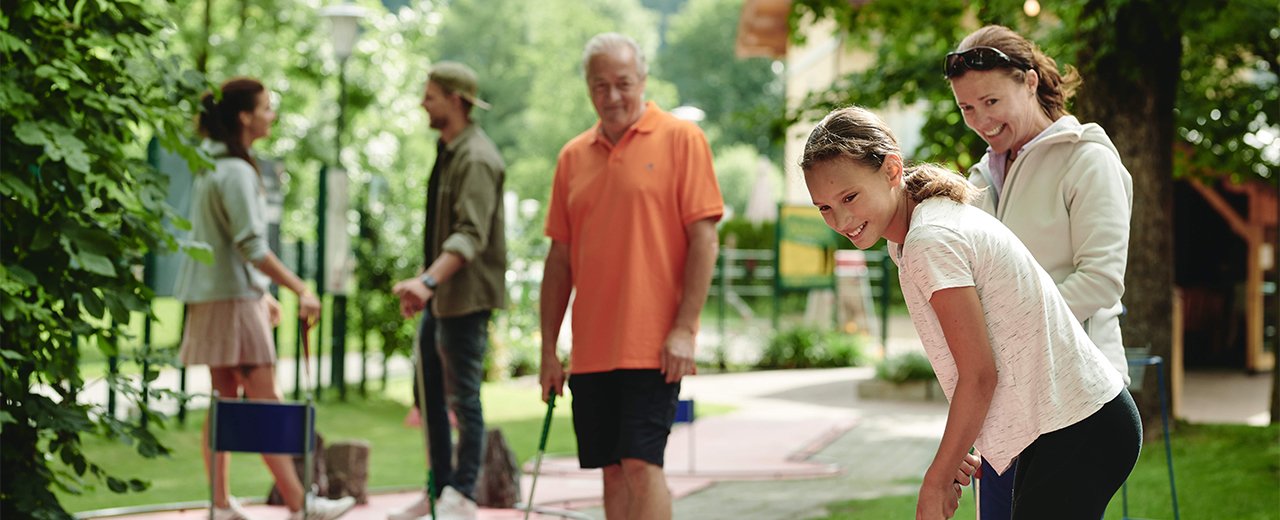 Eine fröhliche Gruppe von Menschen spielt Minigolf in einem grünen Park, umgeben von Bäumen und frischer Luft.