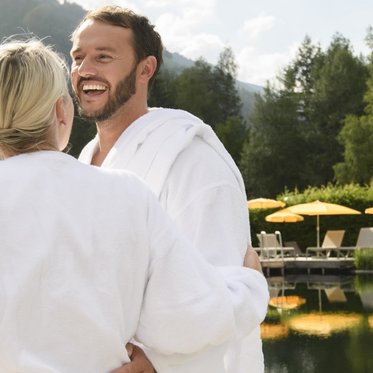 Fröhliches Paar in Bademänteln vor dem Naturbecken einer Therme in Gastein