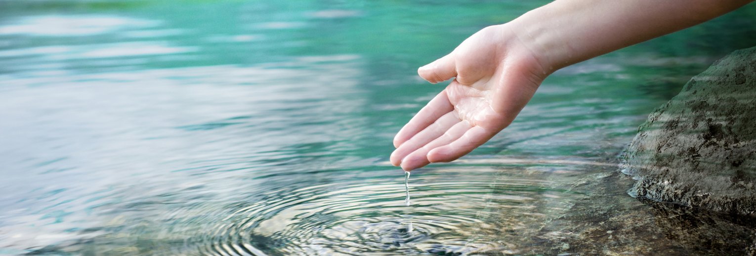 Hand einer Person vor der Wasseroberfläche eines Sees