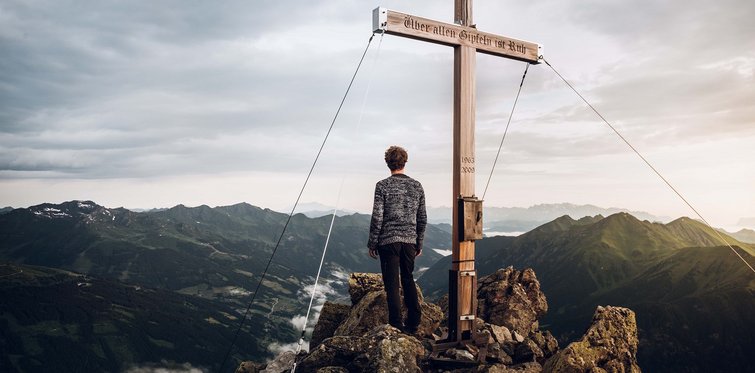 Wanderer am Gipfelkreuz auf einem Berg im Gasteinertal mit weitem Panorama über die Alpenlandschaft der Hohen Tauern.