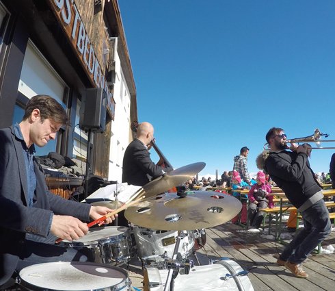 Jazzmusiker auf der Terrasse einer Skihütte vor Publikum auf Bierbänken