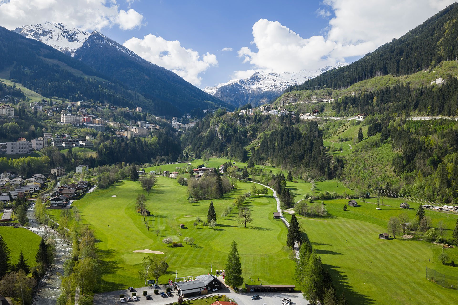 Eine weite, grüne Landschaft mit sanften Hügeln, umgeben von schneebedeckten Bergen und einem klaren blauen Himmel.