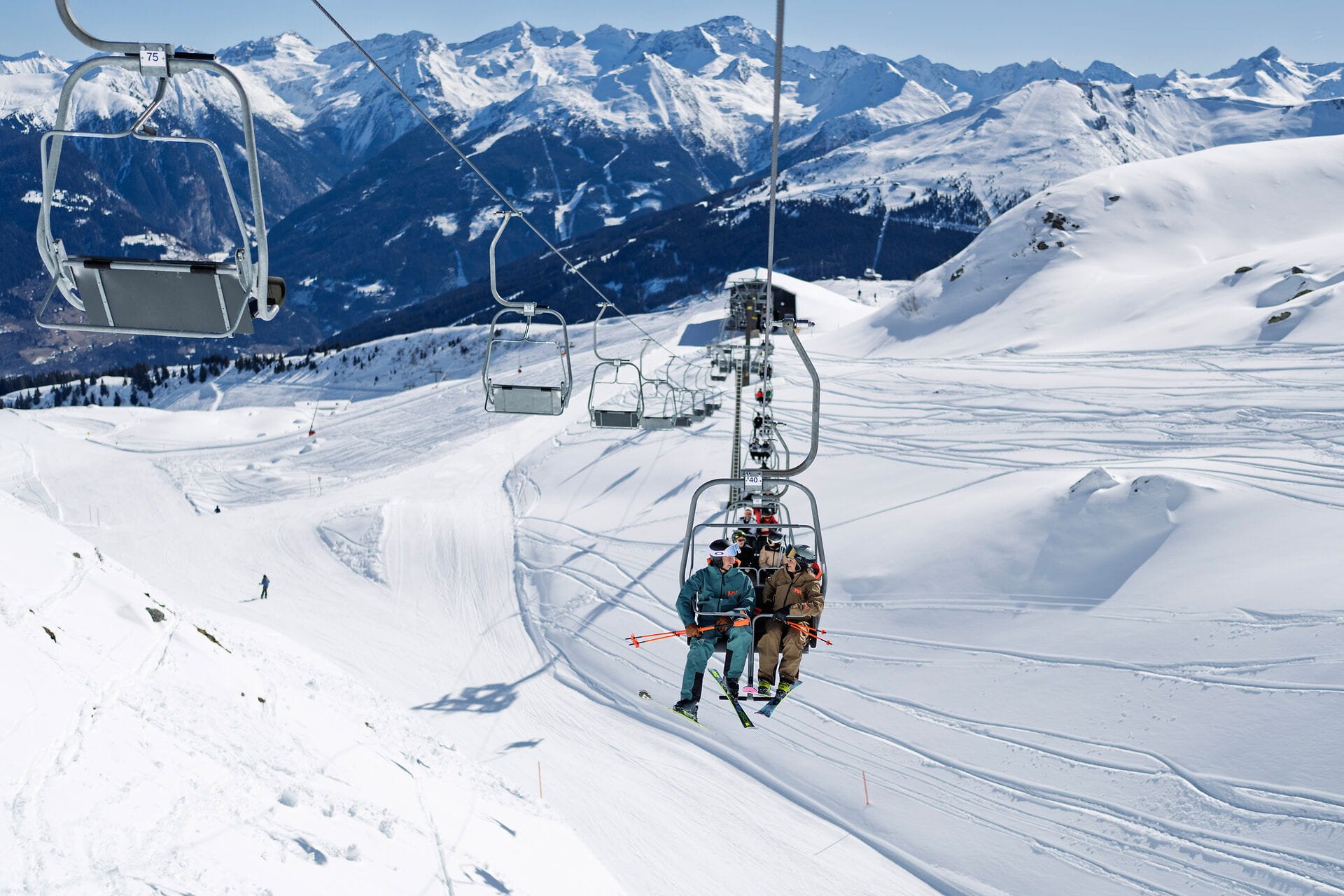Skifahrer und Skifahrerin im Sessellift auf der Schlossalm im Gasteinertal mit Blick auf verschneite Alpen