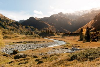Herbstliche Berglandschaft im Gasteinertal mit alpinem Fluss im Vordergrund und warmem Sonnenlicht über den umliegenden Gipfeln.